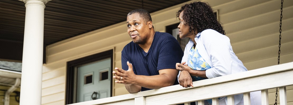 Black man and woman leaning on the railing of a house