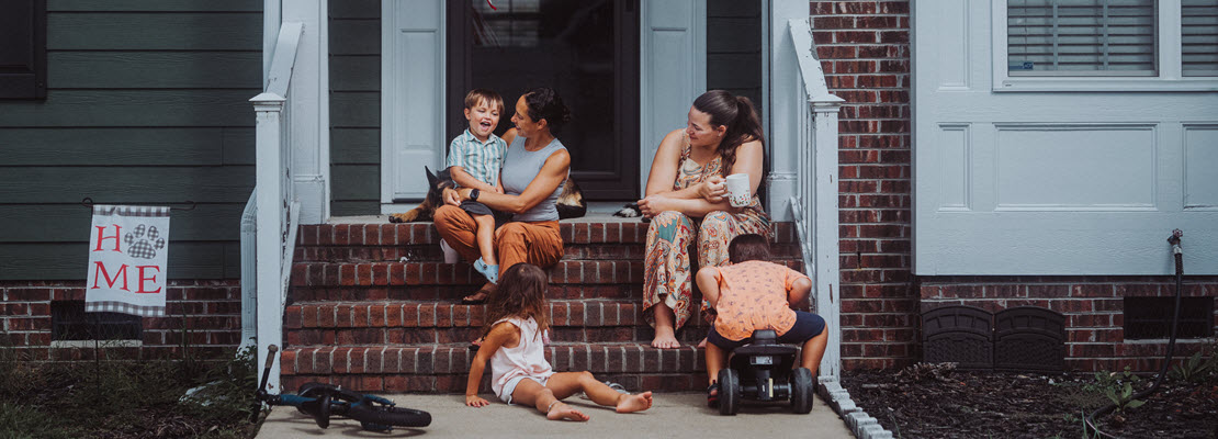 Two women, three young children and a dog sitting on or in front of brick steps to a home