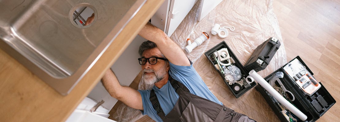 Man making repairs under kitchen sink