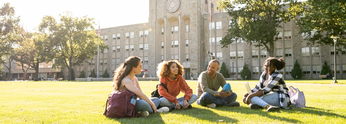 Four college students sitting on a front lawn of a college campus building