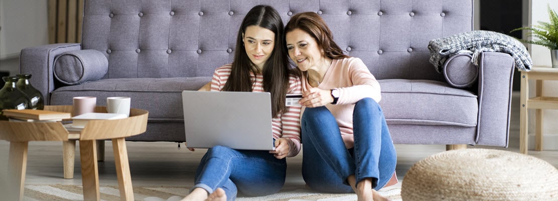 two women sitting on the floor looking at their laptop
