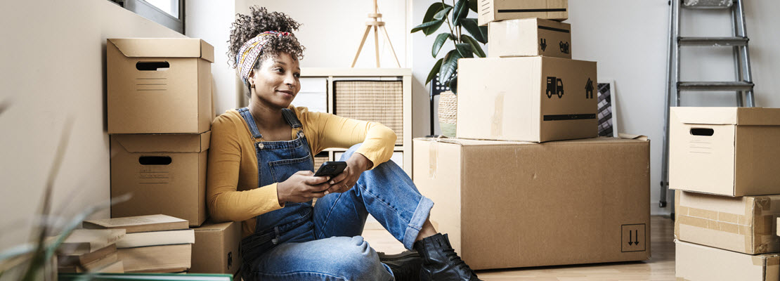 Young Black woman sitting on floor in a home surrounded by closed cardboard boxes