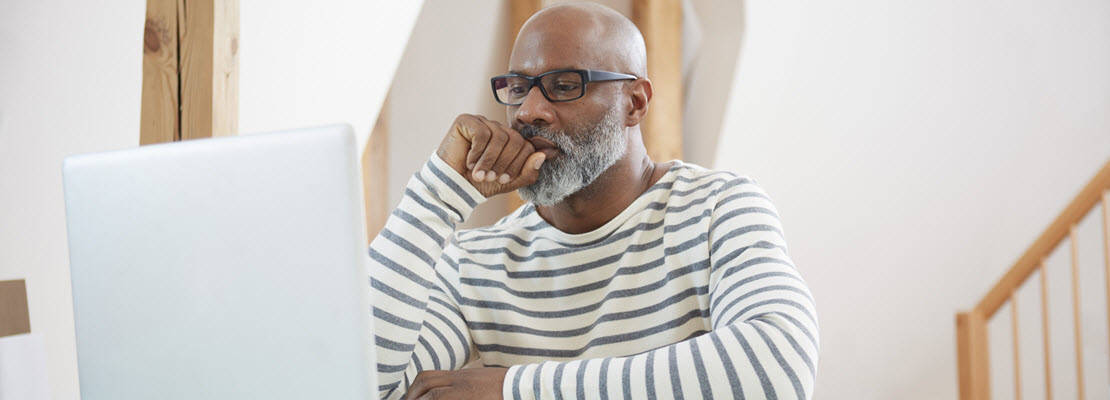 Bald, older Black man with a black and white beard and mustache, wearing black rectangular glasses looking at laptop computer screen.