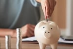 hand putting stacks of coins into piggy bank