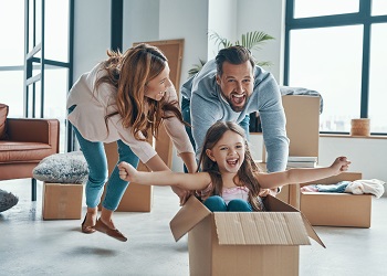 young couple playfully pushing daughter around living room in a moving box