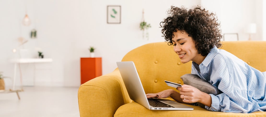 woman laying on sofa looking at laptop and holding credit card