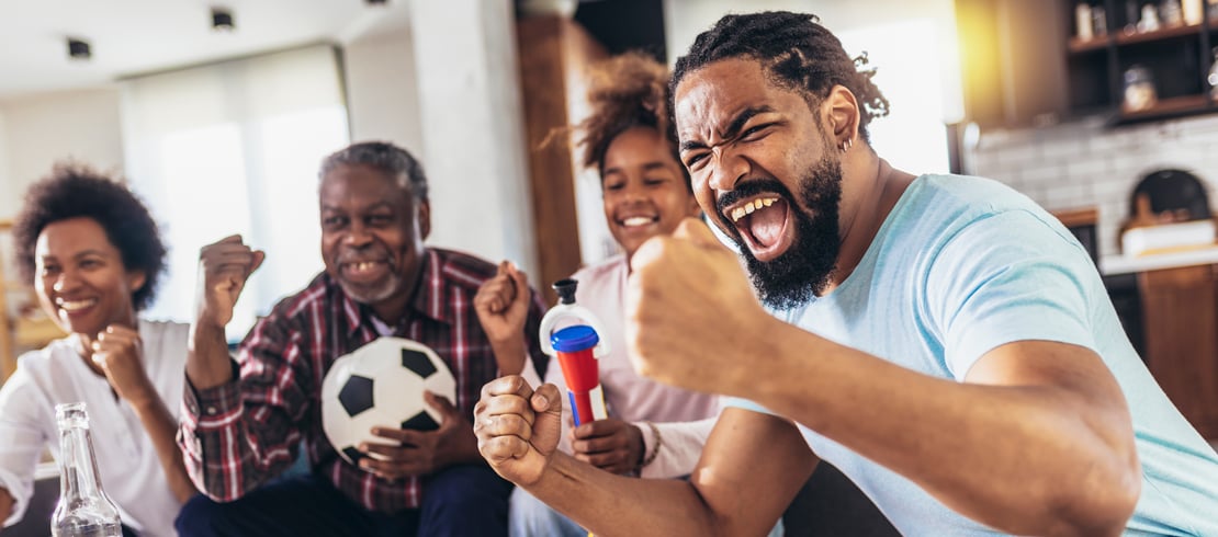 man cheering while watching a soccer match from home