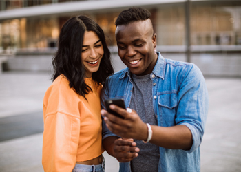 two young adults looking at a shared mobile phone and smiling