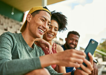 young couple in the stands of a sporting event smiling at a mobile phone