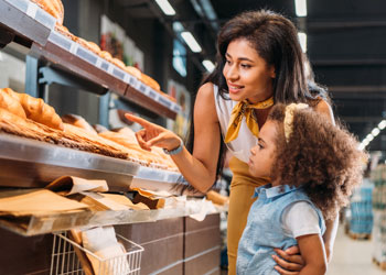 mother and daughter at a grocery store looking at selection of bread