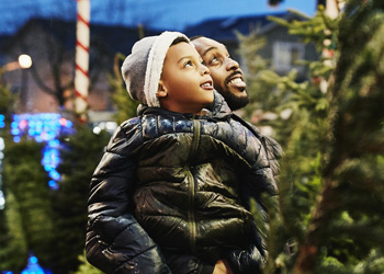 man holding boy while shopping for Christmas trees