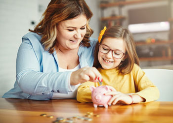 mother helping daughter load a piggy bank