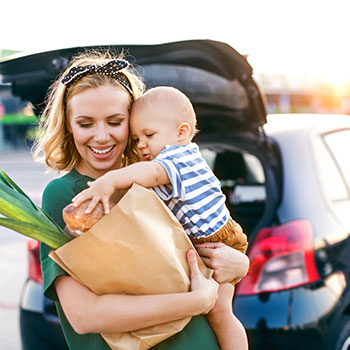 mother holding young child in front of car