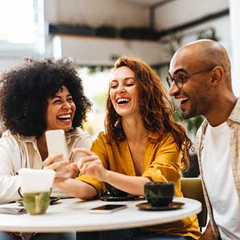 three friends smiling and looking at phone in cafe