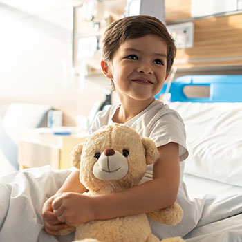 young child in hospital bed holding teddy bear