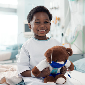 child smiling and holding teddy bear in hospital bed