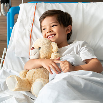 young child holding teddy bear in hospital bed