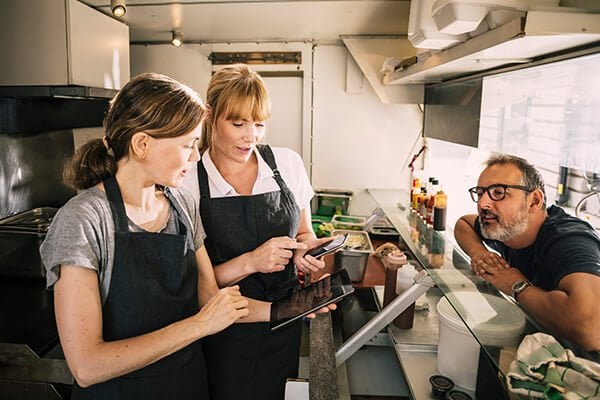 female chefs with technologies while receiving order from man in food truck