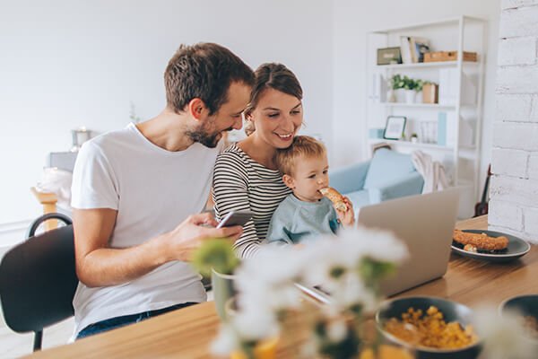  a young family is spending their busy morning over dining table using computer and mobile